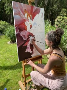 Die Künstlerin Sara Heinrich beim arbeiten an der Staffelei draussen im Garten. Sie malt eine Blüte in rosa auf Leinwand.
